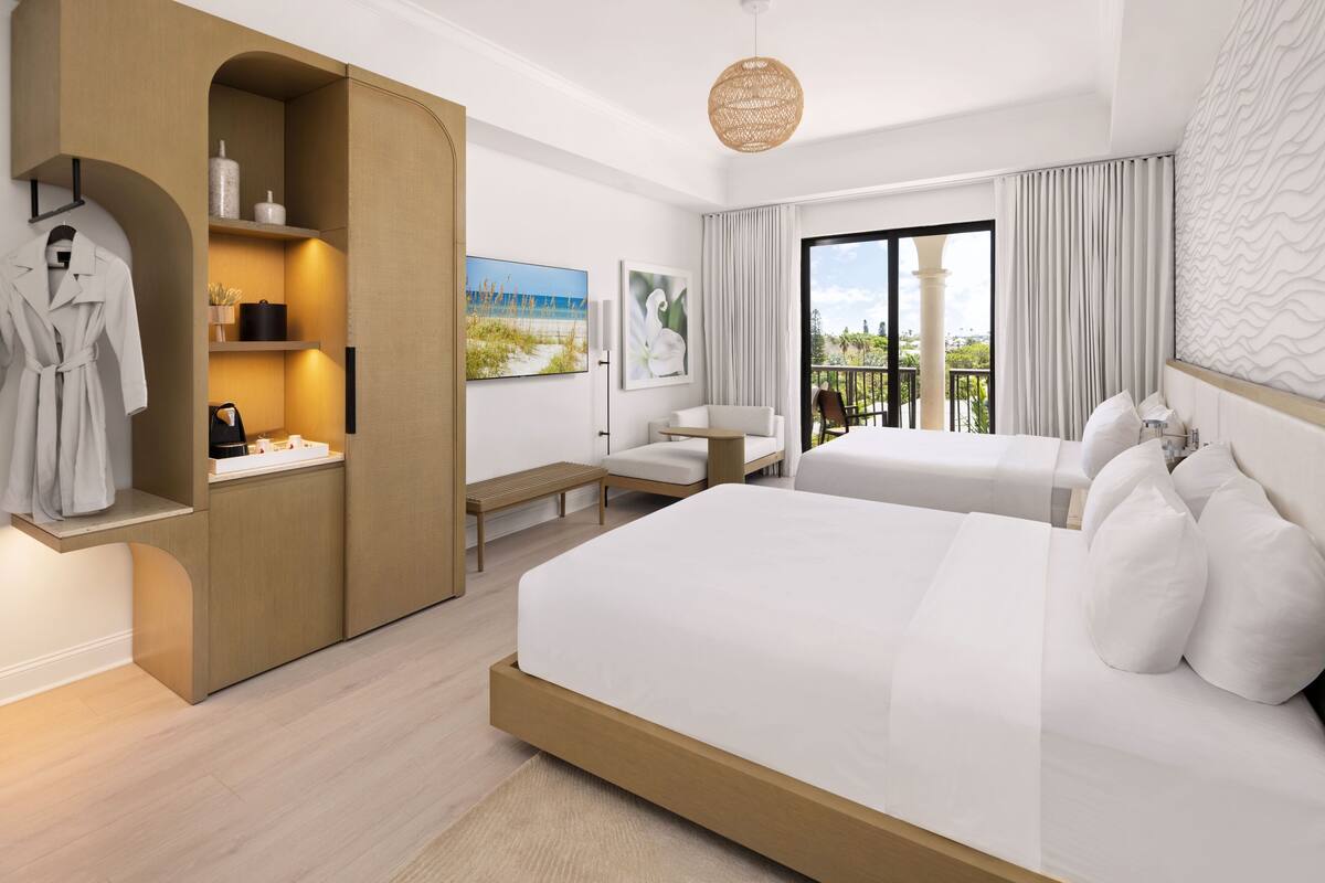 Une chambre d’hôtel moderne dotée d’un grand lit, d’un bureau, d’une chaise et d’un balcon offrant une vue sur la plage.