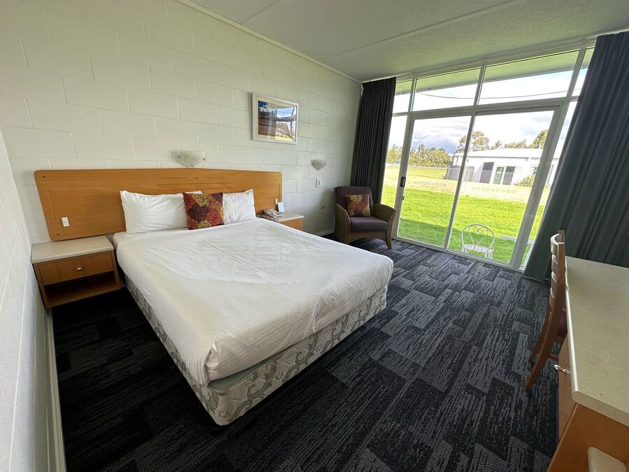 A hotel room with a large bed, a chair, a desk, a window with a view of the outdoors, and a wall-mounted picture.