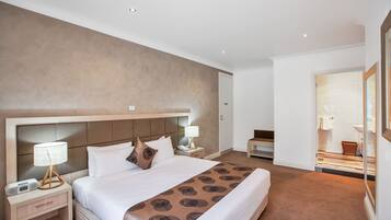 A modern hotel room with a large bed, bedside tables, a nightstand, and a bathroom visible through an open door.