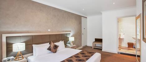 Una habitación de hotel moderna con una cama grande, mesitas de noche y un baño visible a través de una puerta abierta.