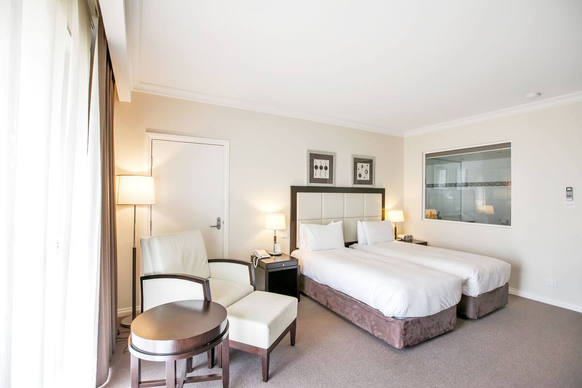 A hotel room with a bed, a chair, a small table, a nightstand, and a lamp.