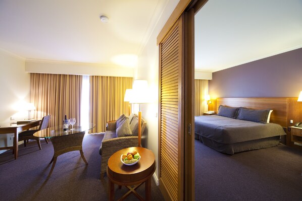 A hotel room with a bed, a sitting area with a glass table and chairs, a small round table with fruit, and a large window with curtains. - Century Inn (Traralgon)