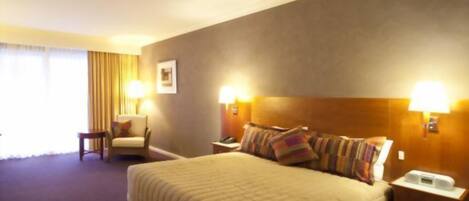 A hotel room with a large bed, two bedside tables, a chair, and a window with curtains.