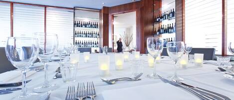 A well-lit dining area with a long table set for a meal, featuring wine glasses, cutlery, and candles.