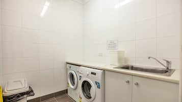 Un lavadero con lavadora, lavamanos y cubo de basura.
