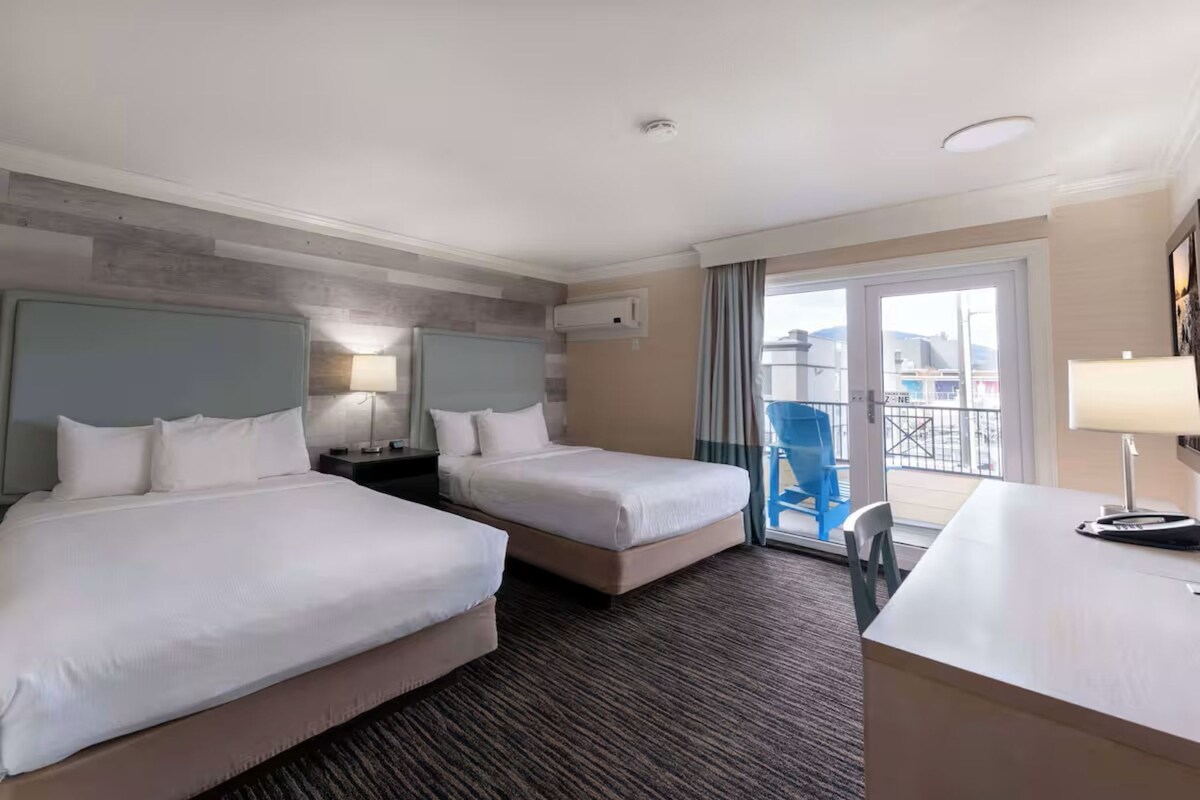 Ein Hotelzimmer mit zwei Betten, einem Schreibtisch, einem Stuhl, einer Lampe und Blick nach außen.
