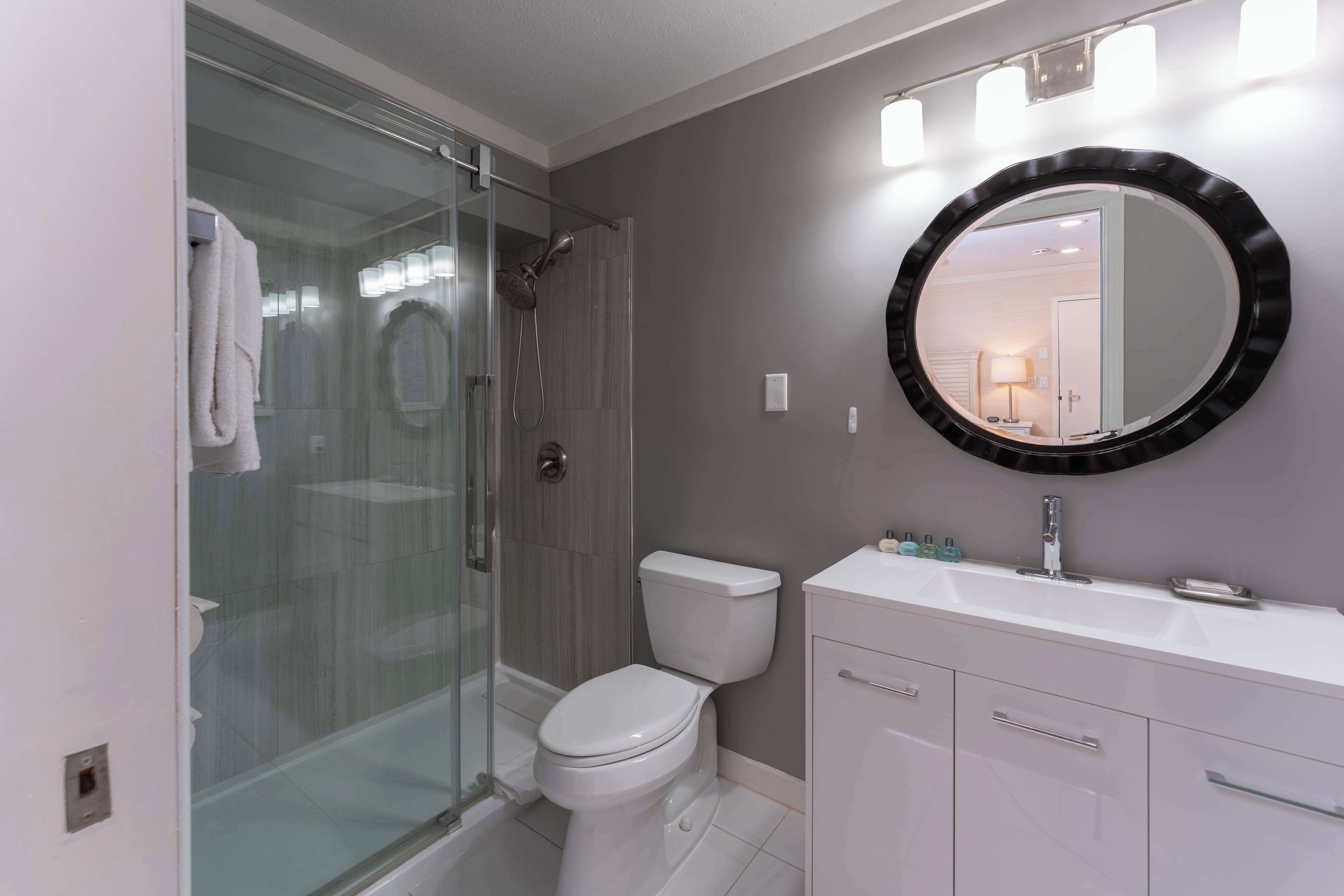 Une salle de bain avec une douche à parois de verre, des toilettes blanches, un meuble-lavabo avec un miroir et un évier.