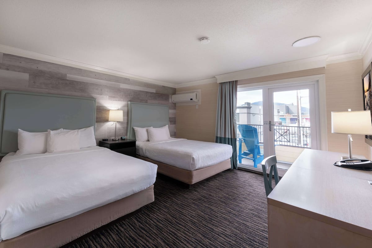 A hotel room with two beds, a desk, a chair, a lamp, and a view of the outside.