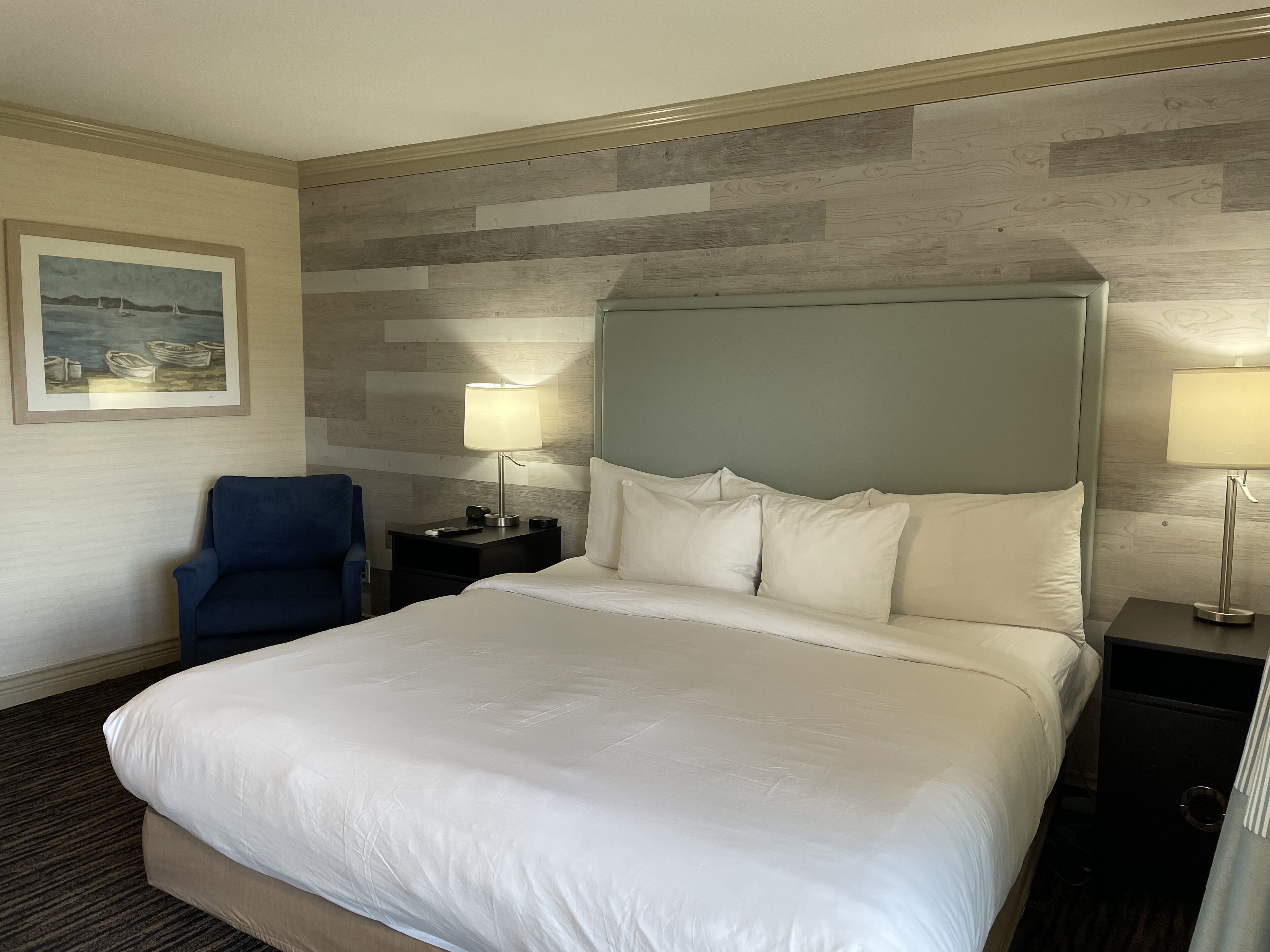 Een hotelkamer met een groot bed, twee nachtkastjes met lampen, een stoel en een schilderij aan de muur.