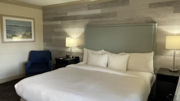 Een hotelkamer met een groot bed, twee nachtkastjes met lampen, een stoel en een schilderij aan de muur.