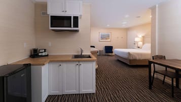 Habitación de hotel compacta con kitchenette, cama, escritorio y una silla.