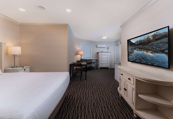 Una habitación de hotel con cama, escritorio, silla, televisor y cómoda.