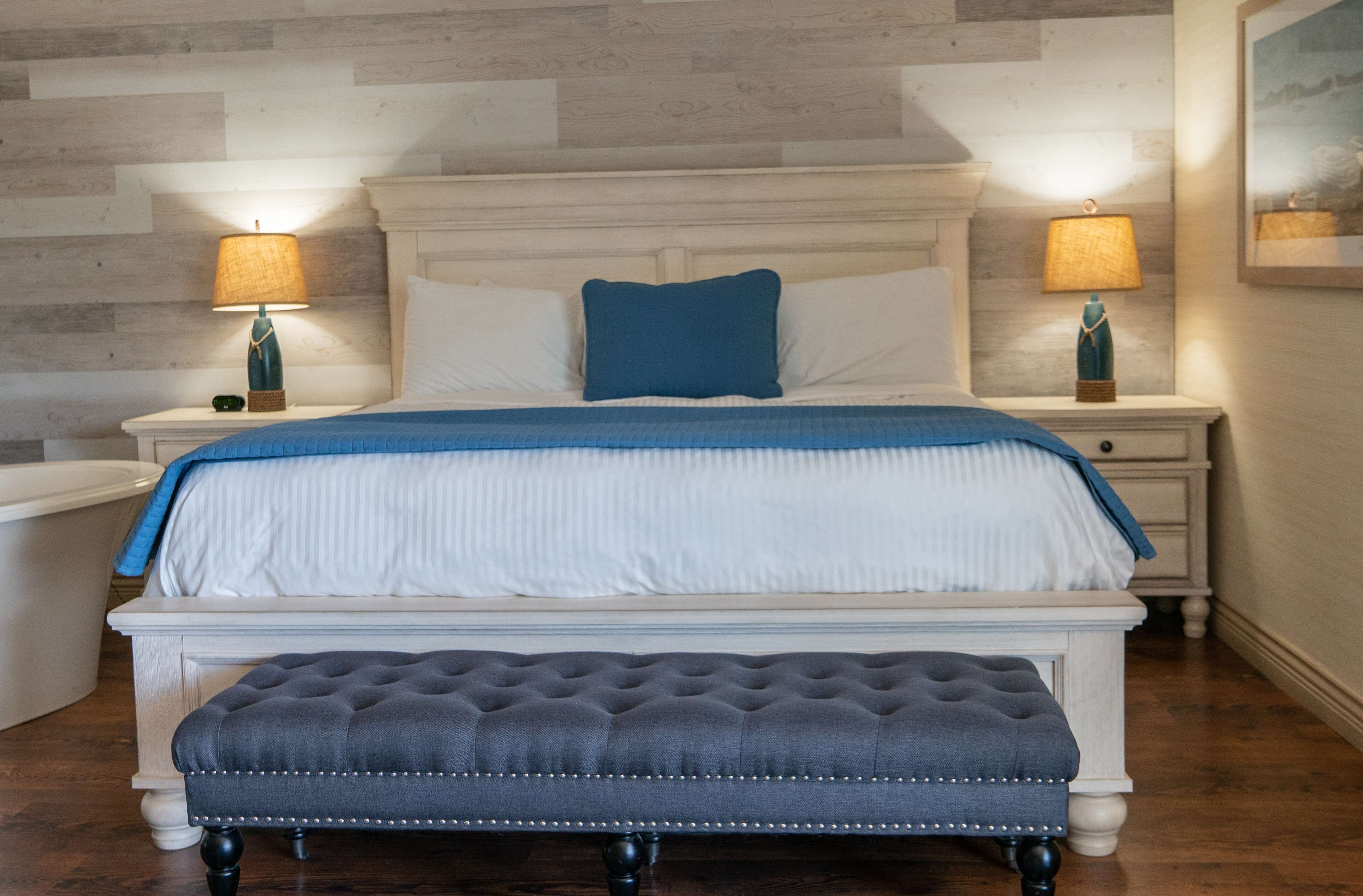 A neatly arranged bedroom with a bed, two bedside tables, a bench, and a wall-mounted lamp.