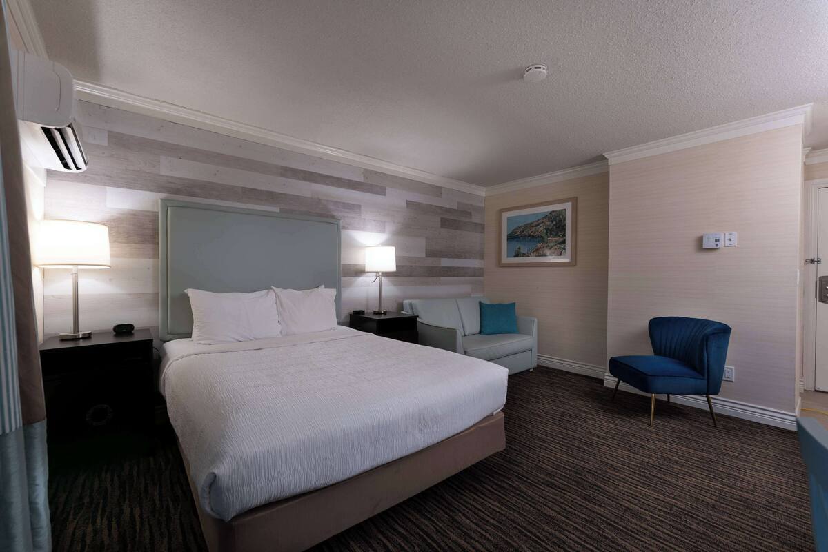 A hotel room with a large bed, two bedside tables with lamps, a chair, and a painting on the wall.