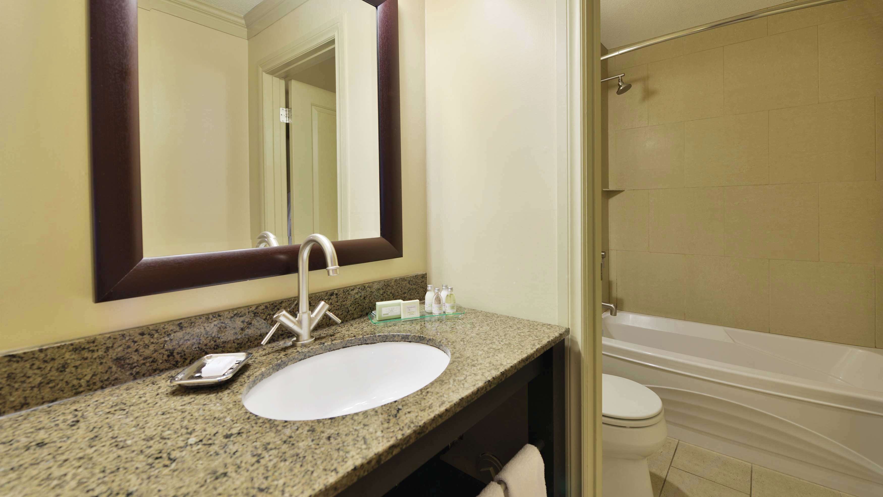 Un baño con encimera de granito, lavabo blanco, espejo y bañera.