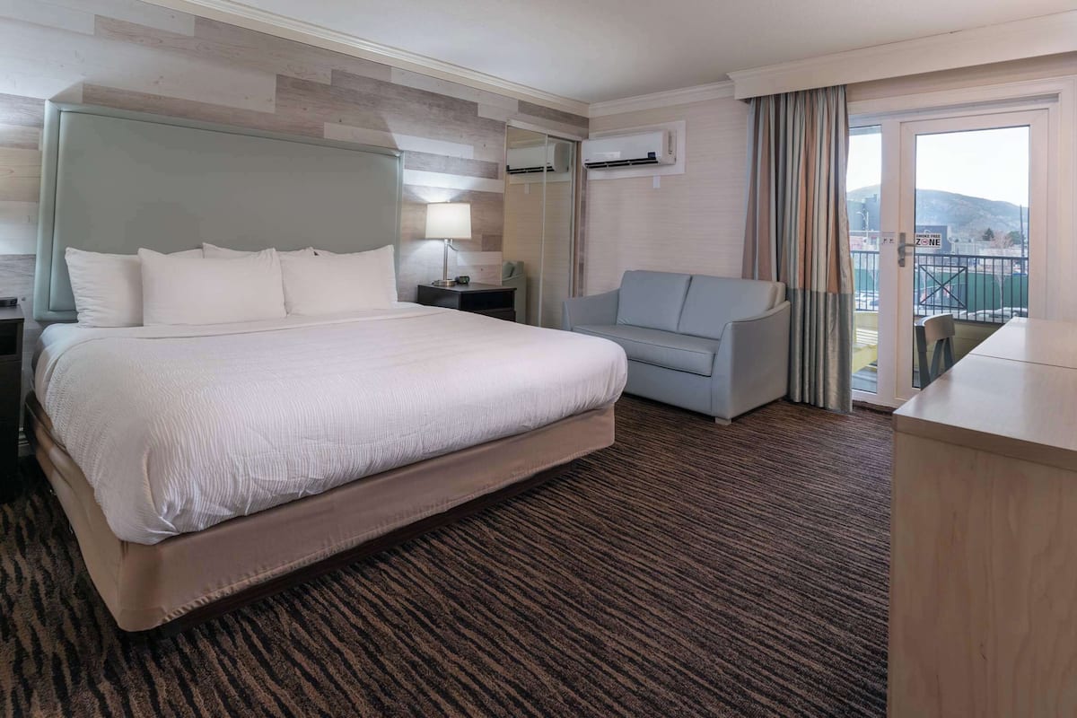 A hotel room with a large bed, a sofa, a desk, and a balcony with a view.