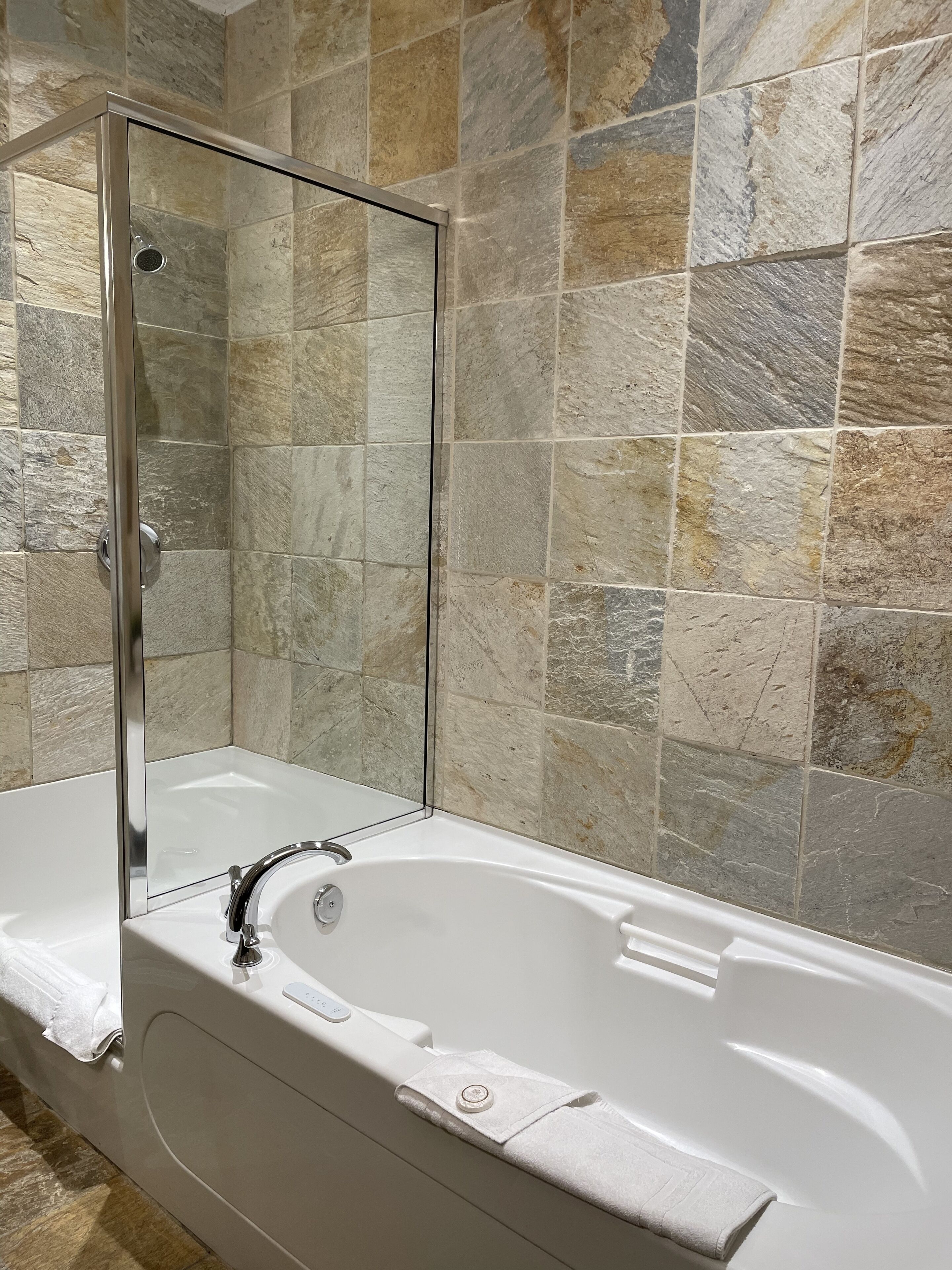 A modern bathroom with a glass-enclosed shower, a white bathtub, and stone-patterned walls.