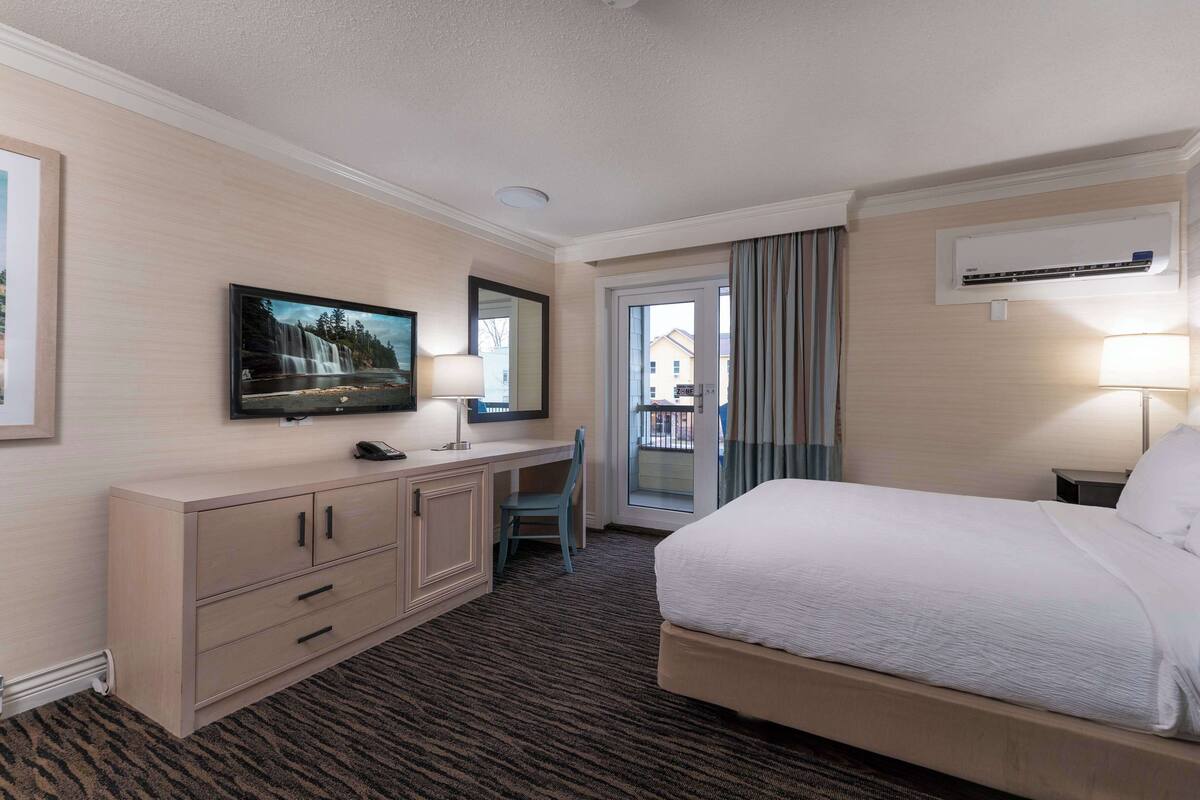 A hotel room with a bed, a desk, a TV, a mirror, and a window with curtains.