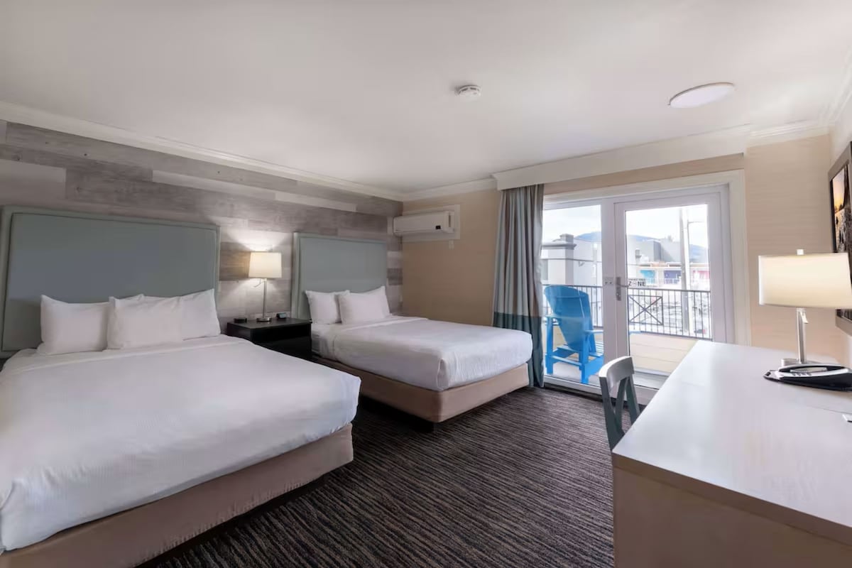 Habitación de hotel con dos camas, un escritorio, una silla, una lámpara y vistas al exterior.