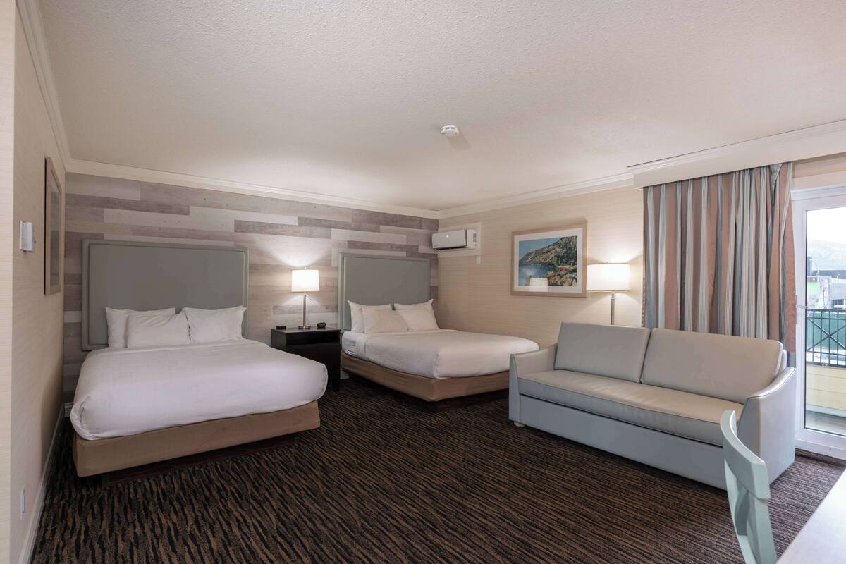A hotel room with two beds, a sofa, a desk, and a window with curtains.
