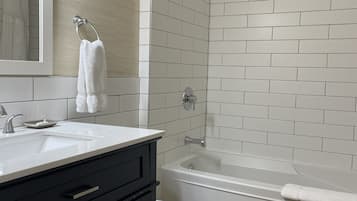 A modern bathroom with a white sink, black vanity, white toilet, and a bathtub with a showerhead.