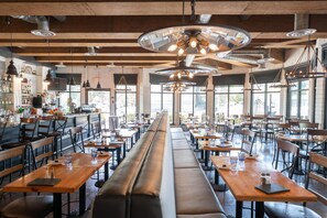 A spacious restaurant with high ceilings, exposed beams, and large windows. Tables and benches are arranged for dining. - Prestige Beach House, WorldHotels Crafted (Kelowna)