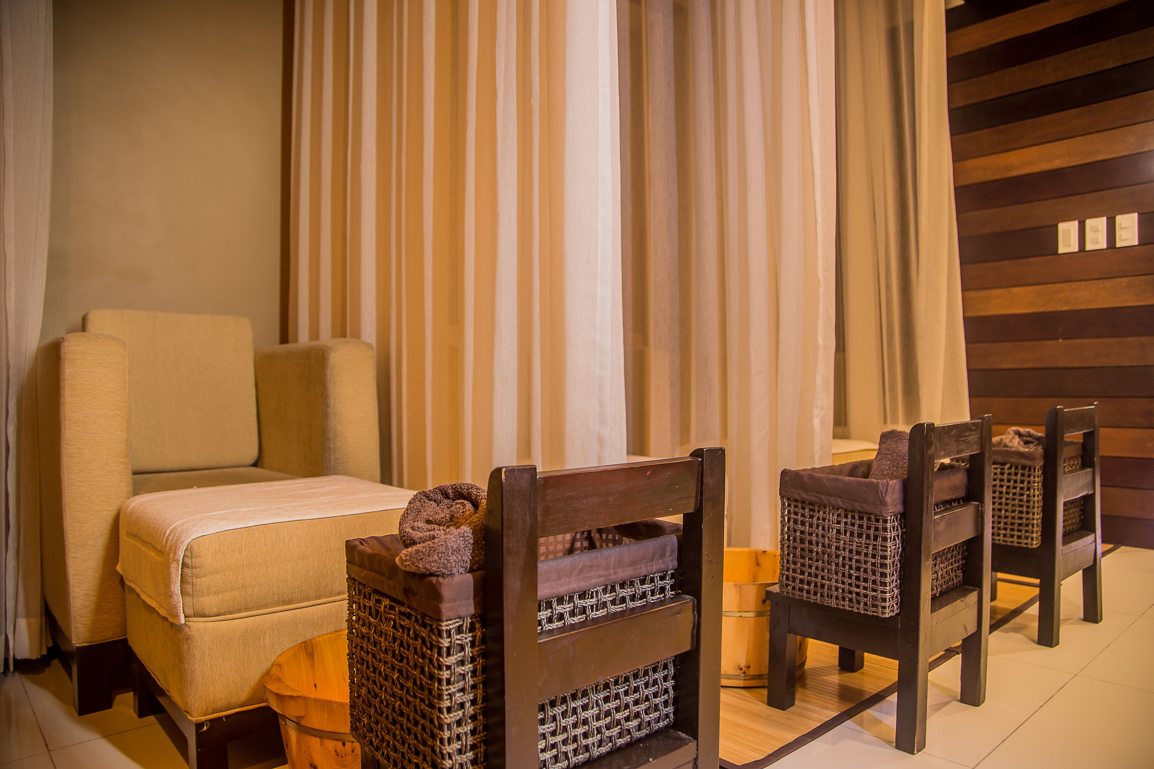 Camera d'albergo con un letto, due poltrone in vimini, un tavolino in legno e un pannello decorativo a tenda.