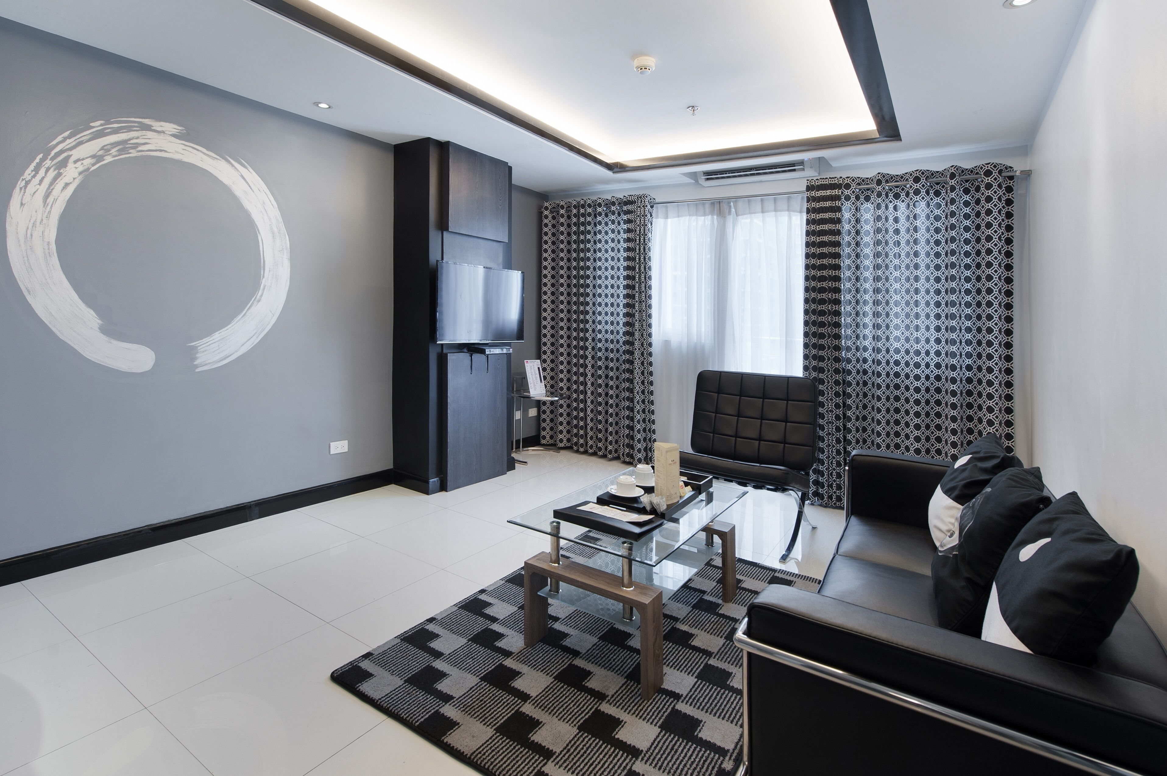 Un salon moderne avec une table basse en verre, un canapé noir et des rideaux à motifs.