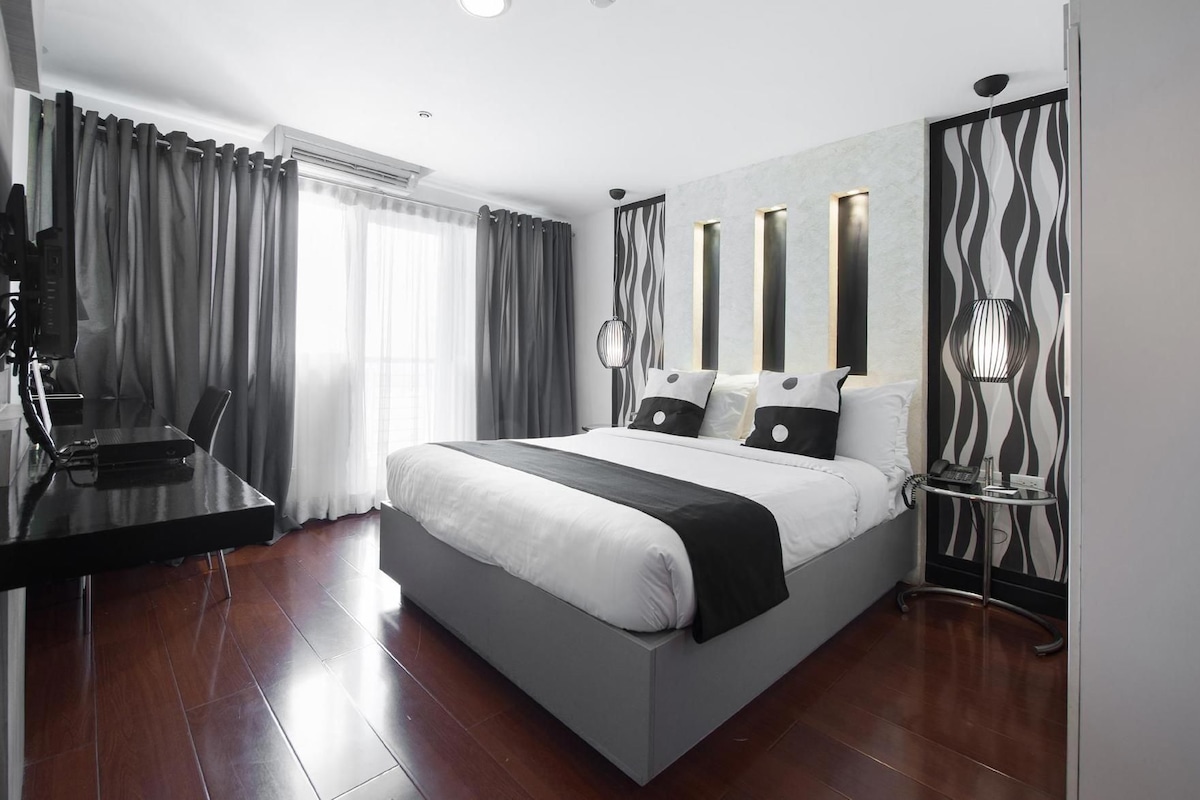 A modern hotel room with a large bed, a desk with a computer, and a telephone.