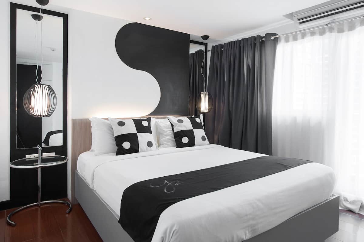 A modern bedroom with a large bed, a bedside table, a mirror, and a hanging light fixture.
