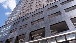 A modern hotel building with a prominent entrance, multiple floors, and a clear sky. - Y2 Residence Hotel managed by HII (Makati)