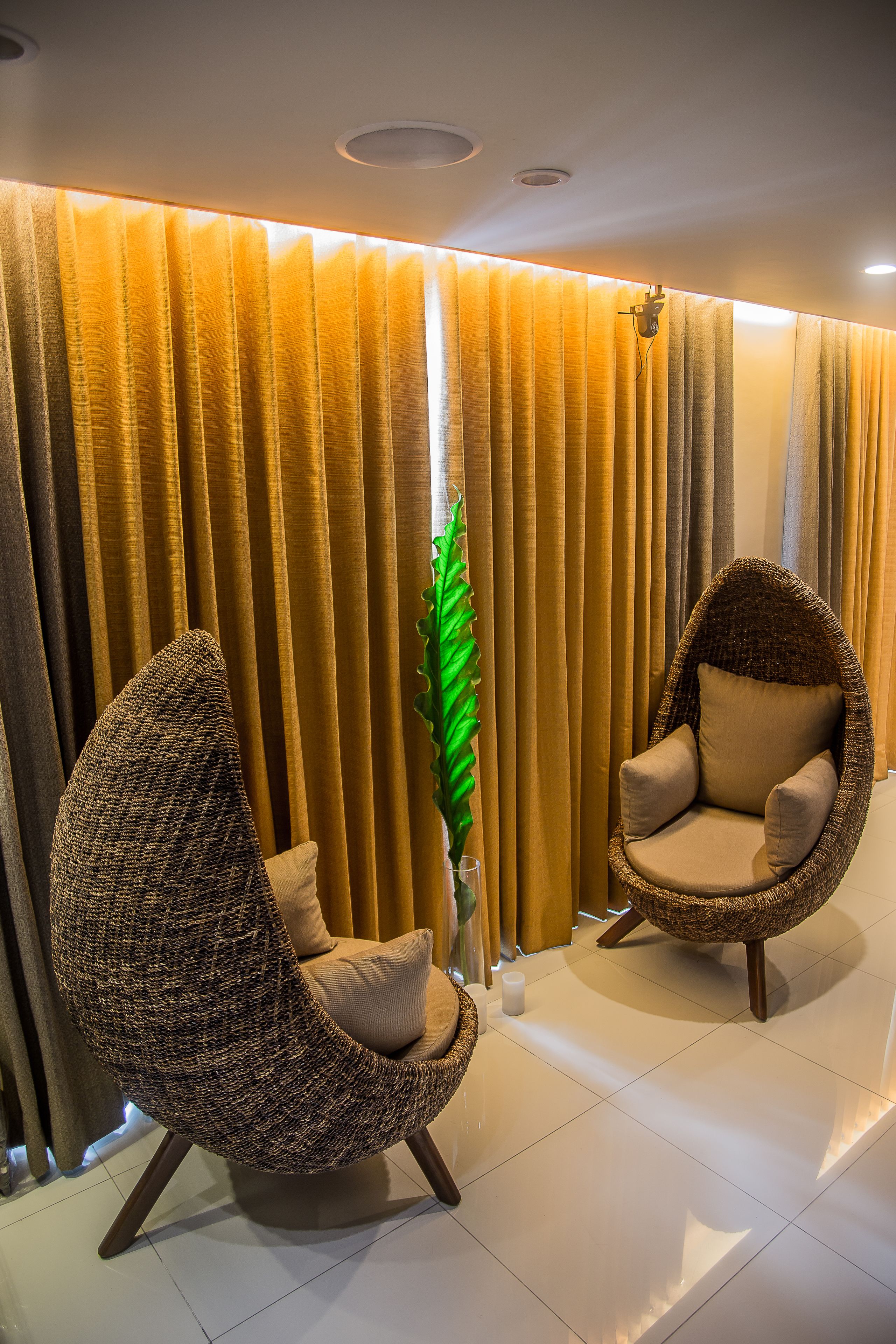 Two wicker chairs with cushions, a potted plant, and a curtain with a light fixture.