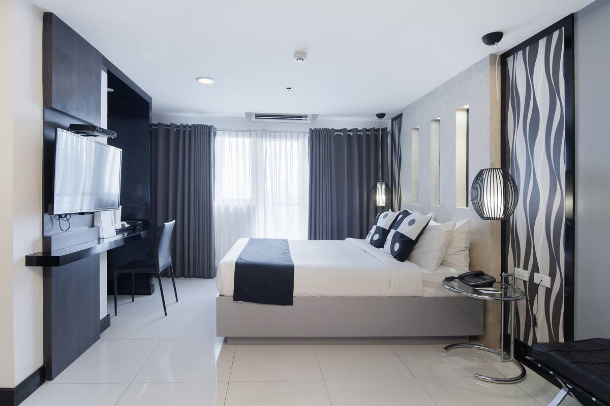 A modern hotel room with a bed, bedside table, and a desk with a chair.