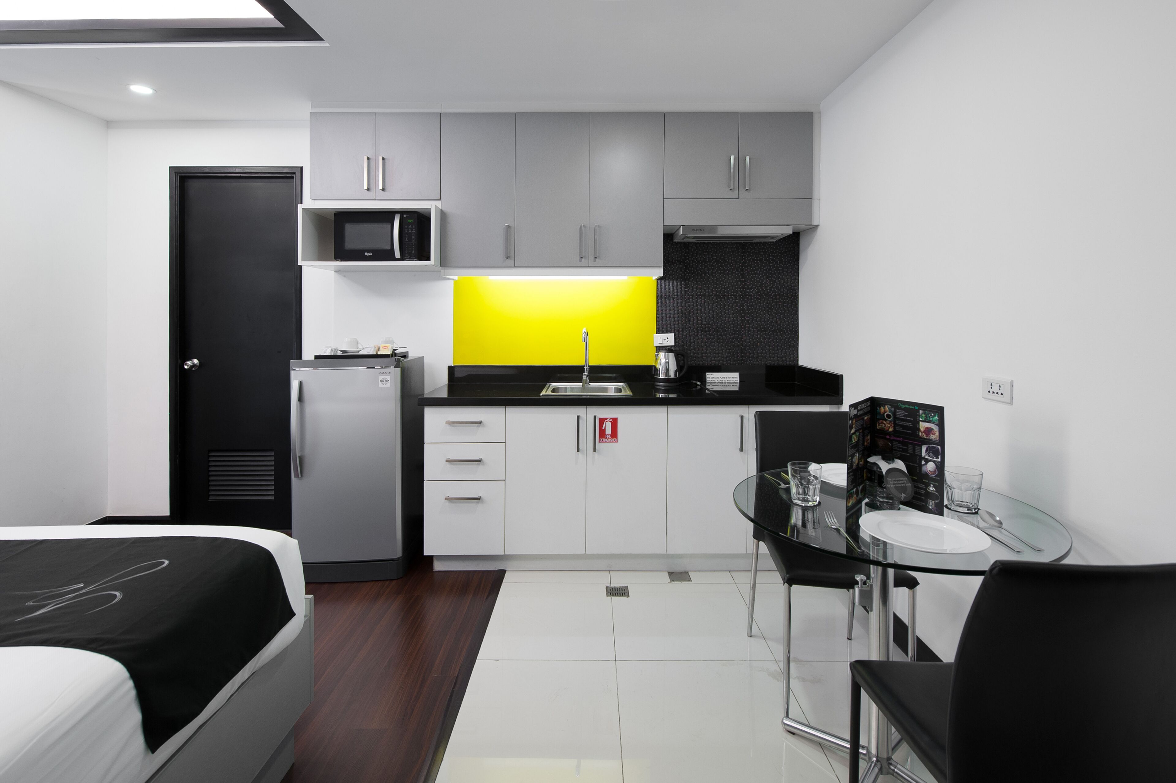 A modern kitchen with grey cabinets, a black countertop, and a yellow backsplash. There is a dining area with a glass table and chairs.