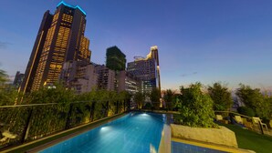A swimming pool surrounded by high-rise buildings, with a clear sky and greenery in the foreground. - Y2 Residence Hotel managed by HII (Makati)