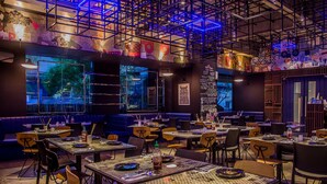 A restaurant with multiple tables and booths, a high ceiling with exposed beams, and large windows. - Y2 Residence Hotel managed by HII (Makati)