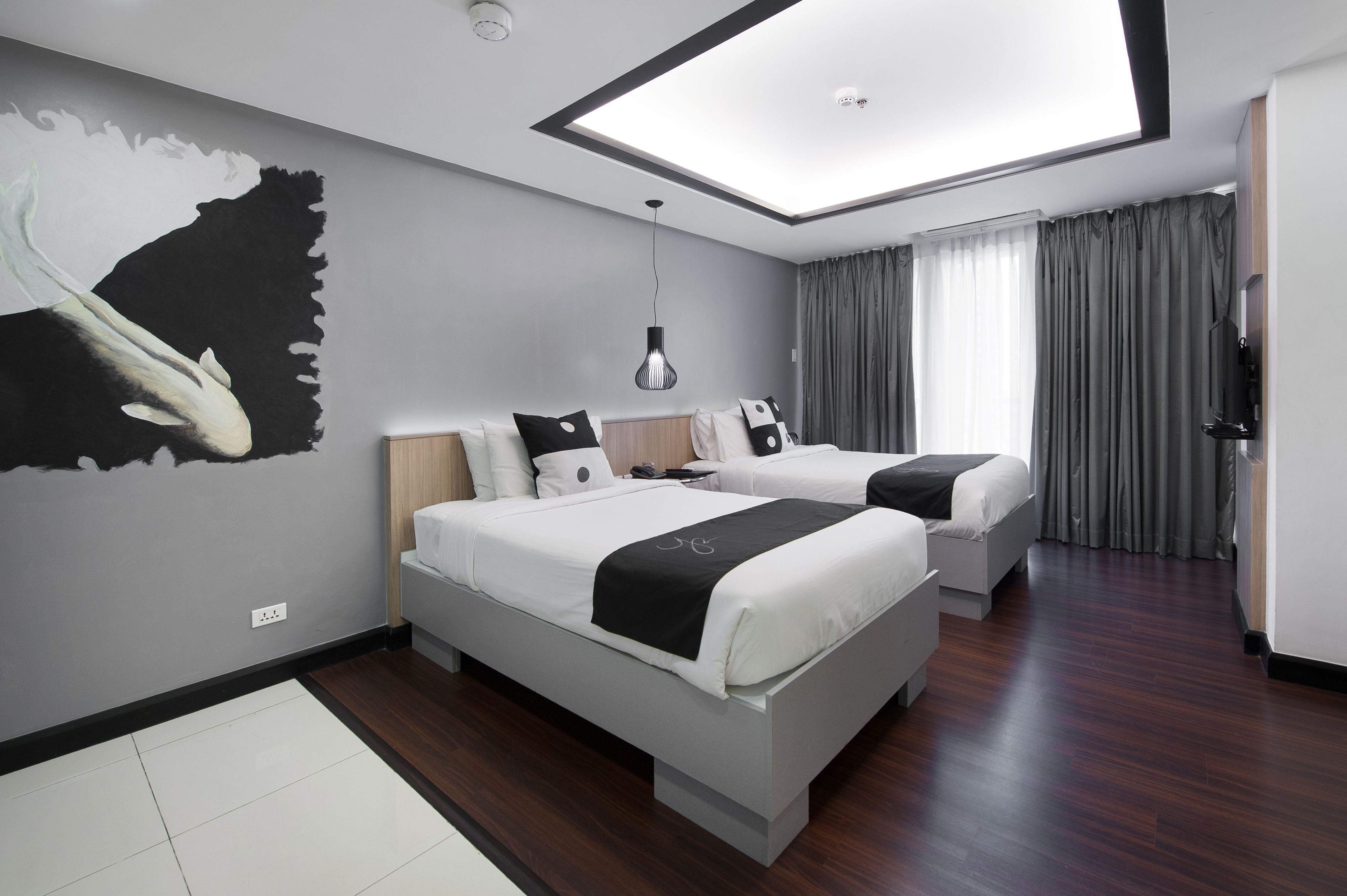 A modern hotel room with two beds, a skylight, a large abstract painting, and a view of the city.