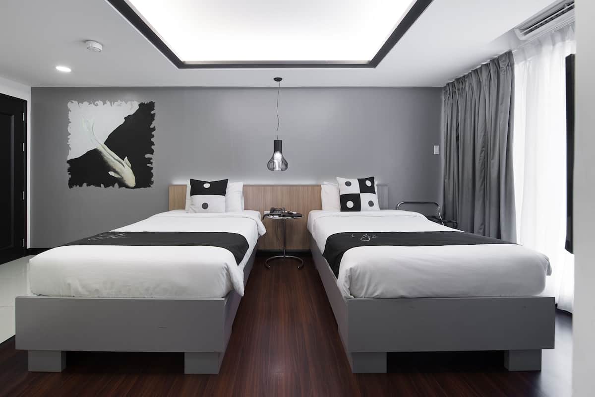 A modern hotel room with two beds, a skylight, a wall mural, and a bedside table.