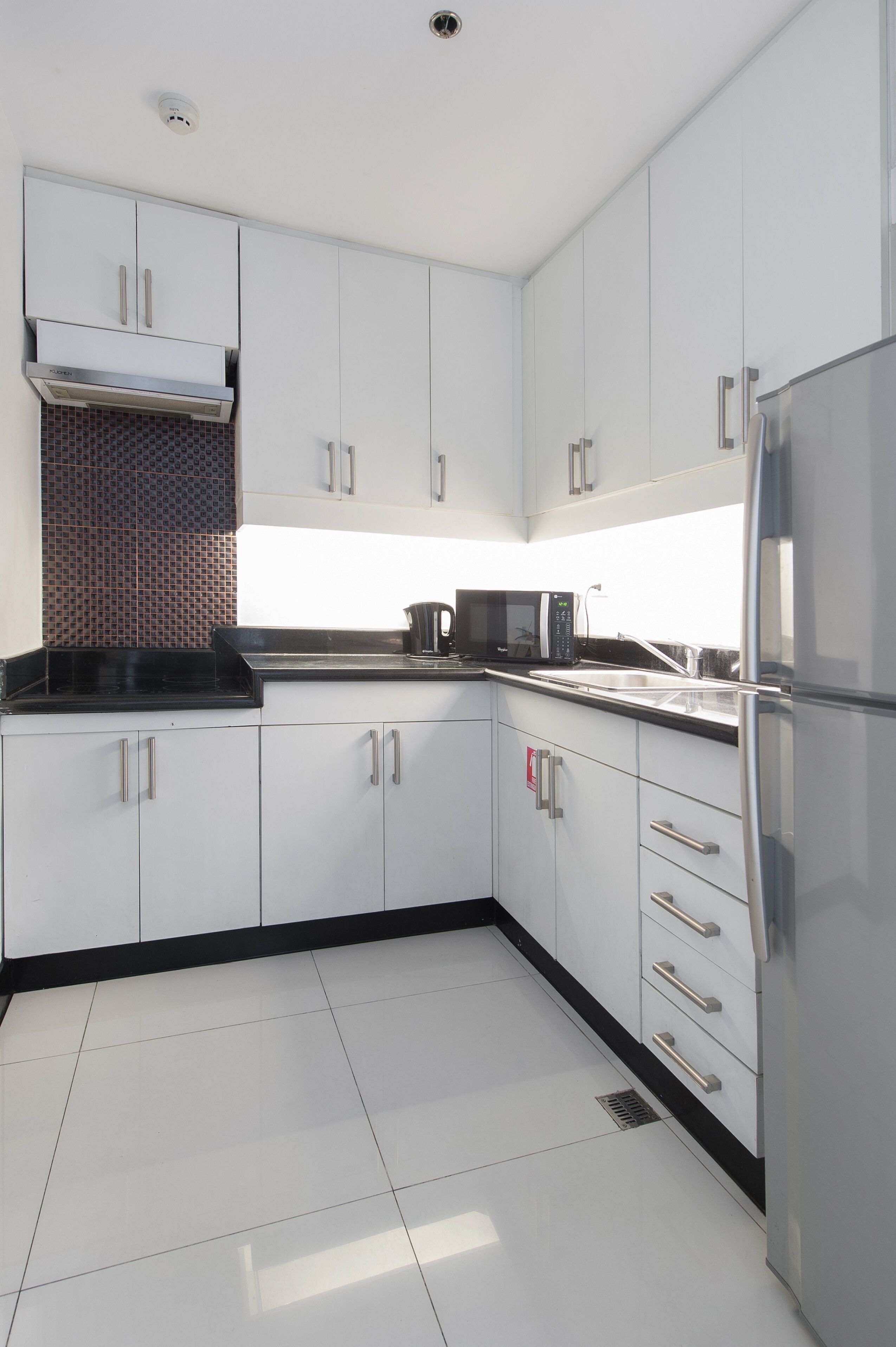 A modern kitchen with white cabinets, a stainless steel refrigerator, and a black countertop.