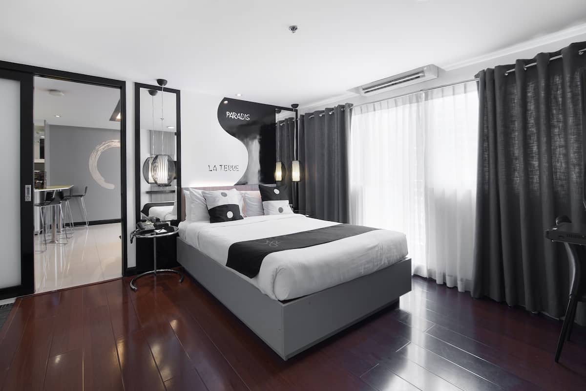 A modern hotel room with a large bed, a desk with a chair, a mirror, and a view of the outdoors.