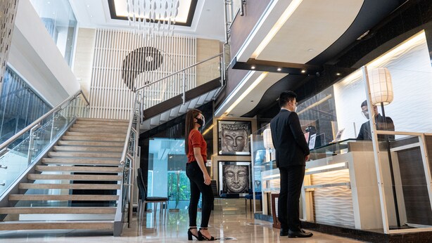 A modern hotel lobby with a glass staircase, a reception desk, and a Buddha statue. - Y2 Residence Hotel managed by HII (Makati)