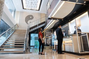 A modern hotel lobby with a glass staircase, a reception desk, and a Buddha statue. - Y2 Residence Hotel managed by HII (Makati)