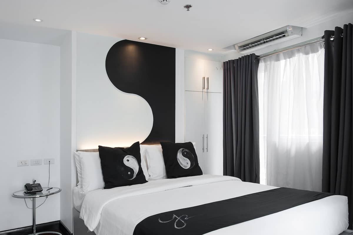 A modern bedroom with a large bed, a bedside table, and a wall-mounted air conditioning unit.