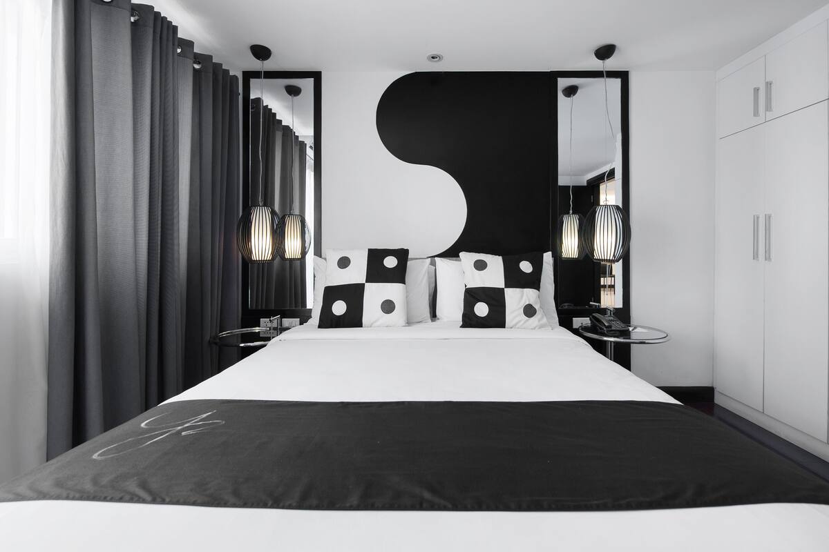 A modern bedroom with a large bed, black and white pillows, a large mirror, and a unique wall design.