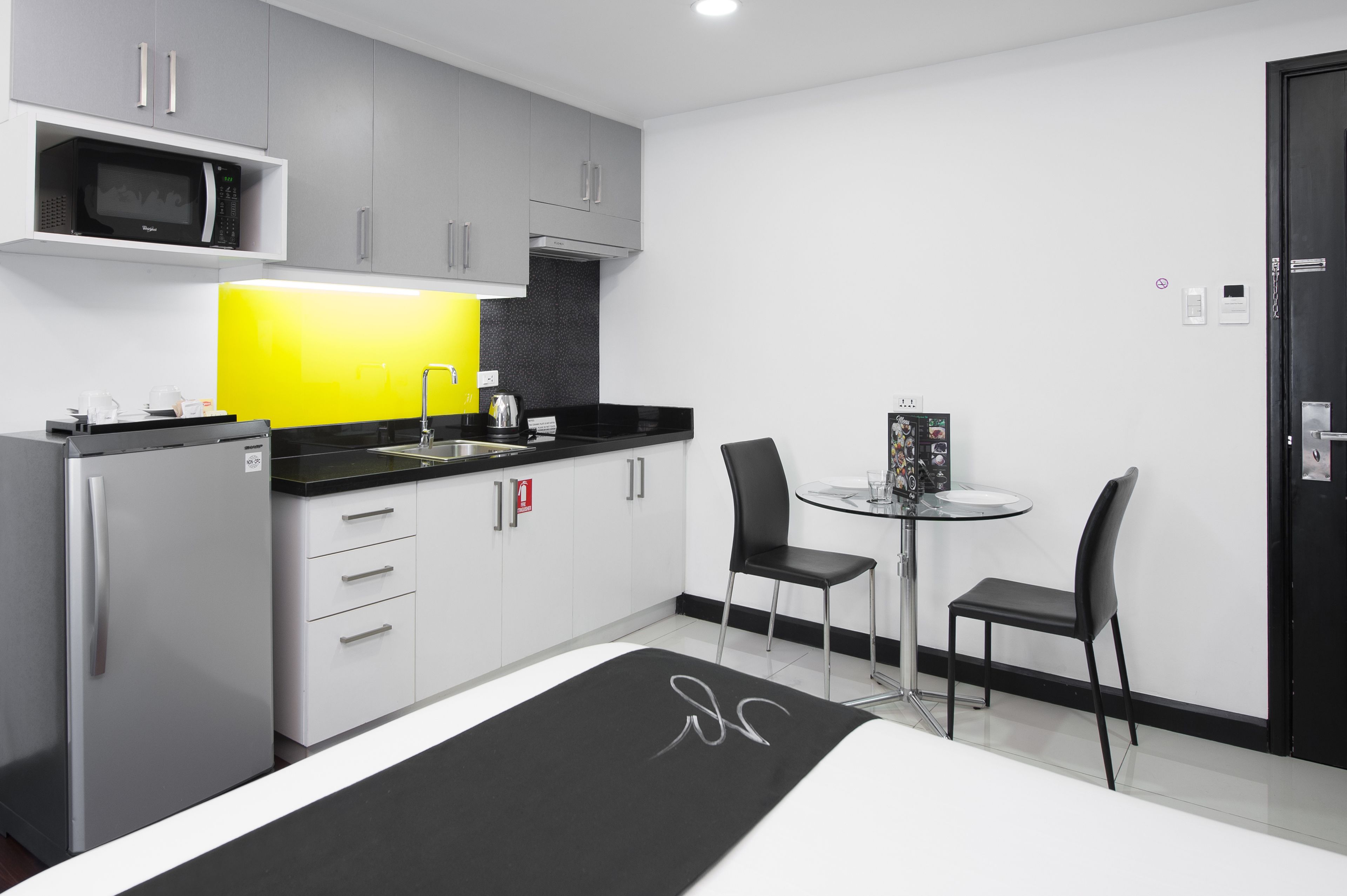 Una cocina moderna con armarios grises, una encimera negra, un microondas y una pequeña zona de comedor con dos sillas y una mesa.