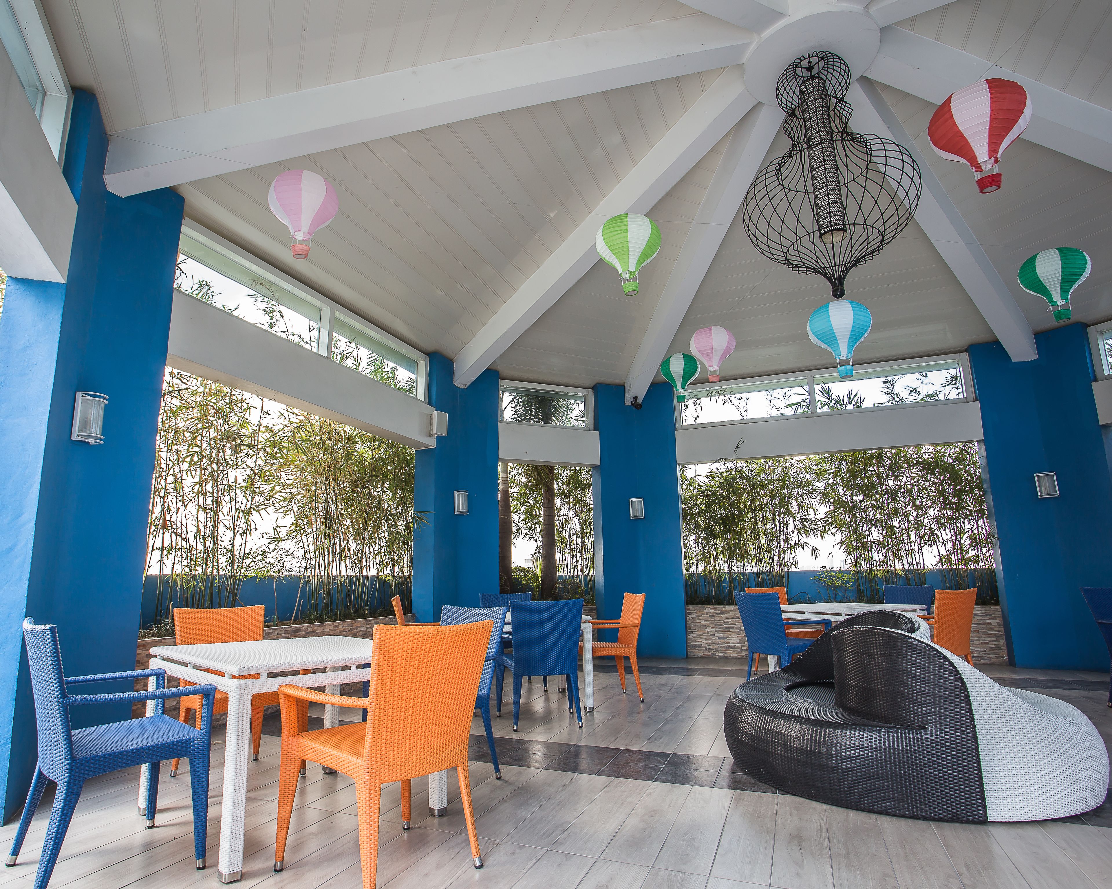 A covered outdoor seating area with tables and chairs, a wicker sofa, and decorative hot air balloons.