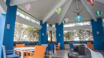 A covered outdoor seating area with tables and chairs, a wicker sofa, and decorative hot air balloons.