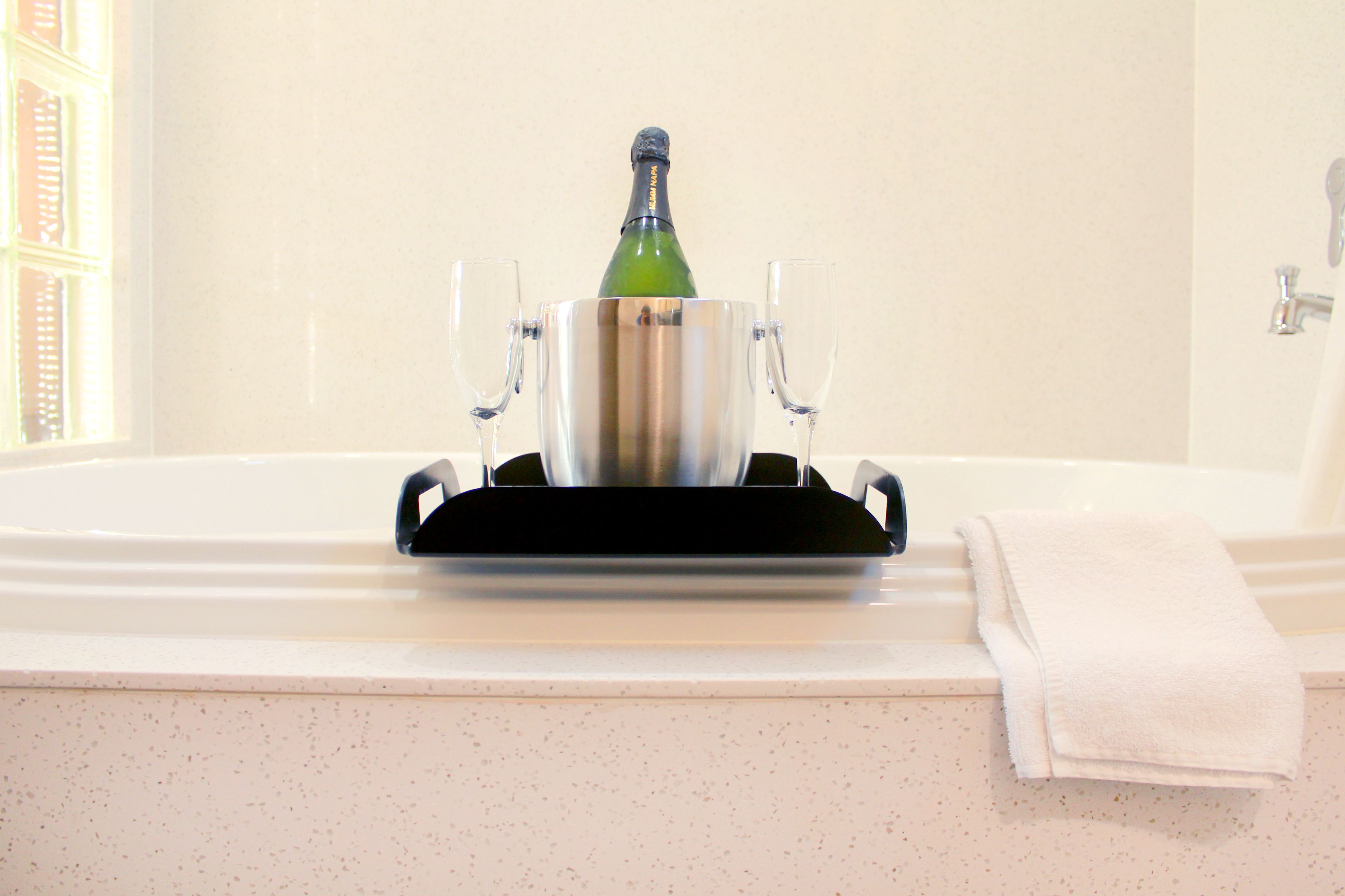 A champagne bottle in a metallic holder on a bathroom counter with two glasses and a towel.