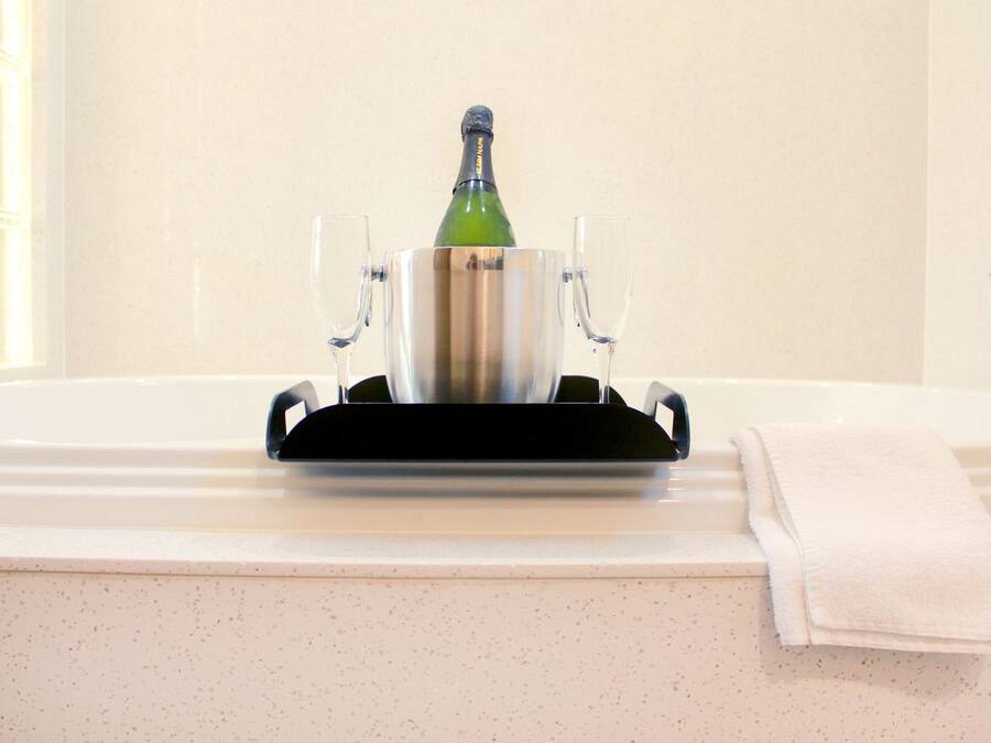 Une bouteille de champagne dans un porte-bouteille métallique, posée sur le comptoir d’une salle de bain, avec deux verres et une serviette.