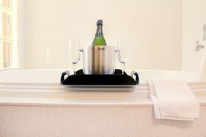 A champagne bottle in a metallic holder on a bathroom counter with two glasses and a towel.